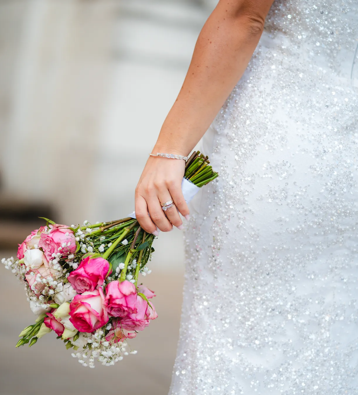 Detailaufnahme: Braut hält einen Strauß aus rosa Rosen und Schleierkraut vor ihrem glitzernden Brautkleid